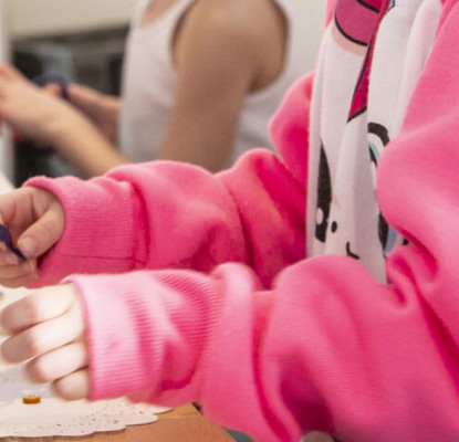 Photograph of a child's arms and hands. They are wearing a white and pink sweatshirt and they are doing a craft. 