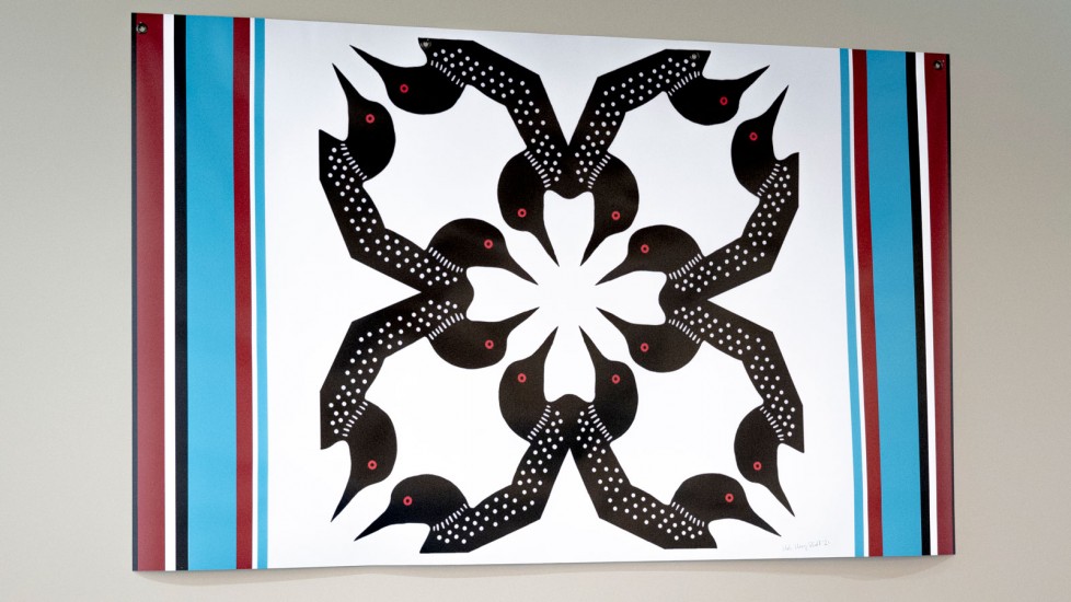 A colourful banner with vertical stripes in red, black, and blue, possibly representing a ribbon shirt design. Eight black loons with white spots and red eyes are arranged in a circular pattern on a white background.
