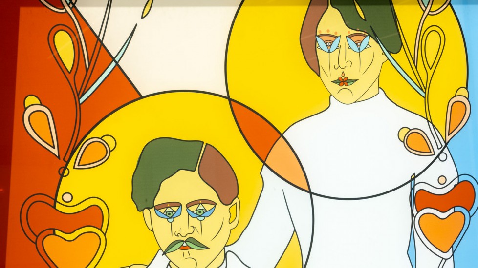 A colourful stain-glass painting featuring two figures with stylized facial features. These figures are set against a backdrop of bold colours and geometric shapes, including circles and heart shapes.