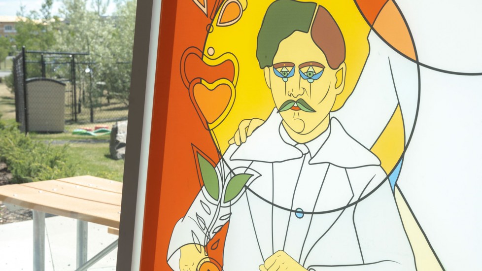 A colourful, stained-glass style artwork featuring a person with stylized features. The artwork is set against a backdrop of a park with trees and a picnic table. 