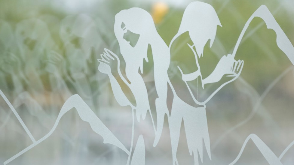 Etched on a glass panel, a man and woman face each other with mountains in the background. The artistic rendering has a soft, dreamlike quality.