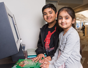 A boy and a girl borrowing a library book using a book scanner.