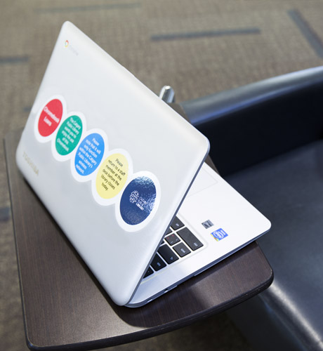An open silver laptop resting on a chair with a desk arm attachment.