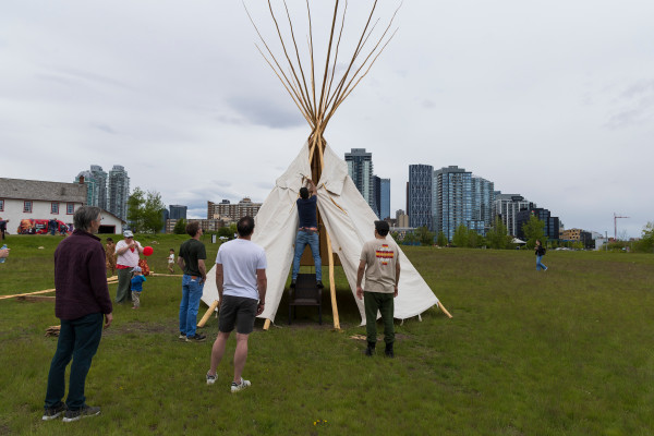 A group of people setting up a tipi on the grass.
