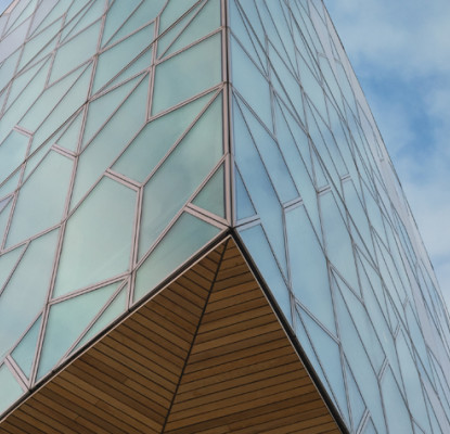 A modern building made of glass with geometrically shaped windows against a blue sky.