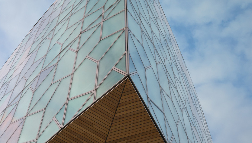 A modern building made of glass with geometrically shaped windows against a blue sky.