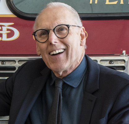 Photograph of Bill Ptacek sitting in front of a fire engine. 