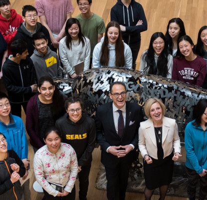A large group of people looking up and standing around a metal sculpture of a bison.