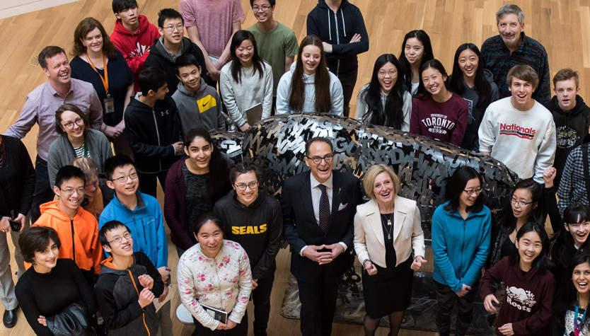 A large group of people looking up and standing around a metal sculpture of a bison.