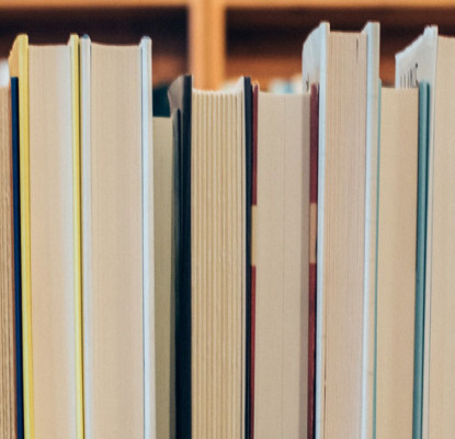 Up close photograph of the pages of books lined up on a shelf. 