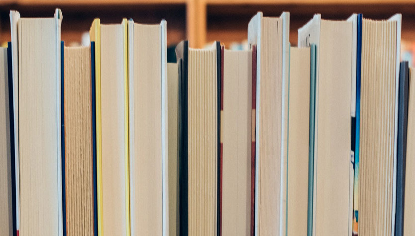 Up close photograph of the pages of books lined up on a shelf. 
