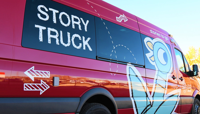 A red van with the text Story Truck on the windows and a large cartoon vinyl pigeon on the doors.