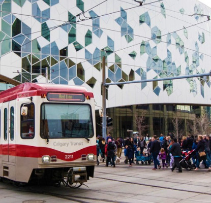 Photo of the exterior of Central Library from the street. A group of people are walking and a train is going by. 