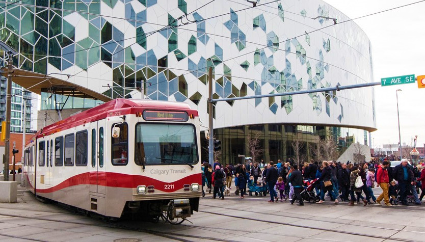 Photo of the exterior of Central Library from the street. A group of people are walking and a train is going by. 