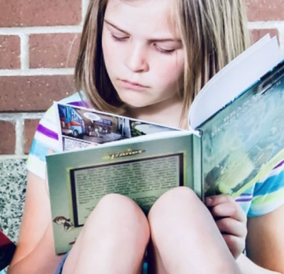 A boy and a girl sitting on a couch reading books.