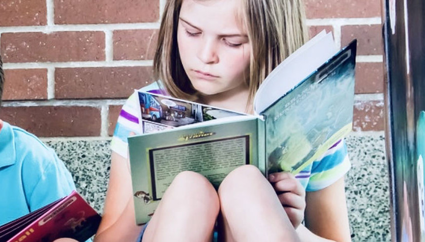 A boy and a girl sitting on a couch reading books.