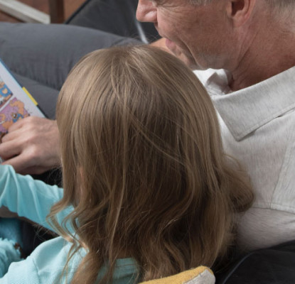 A man and a girl read a book together while sitting on a couch.