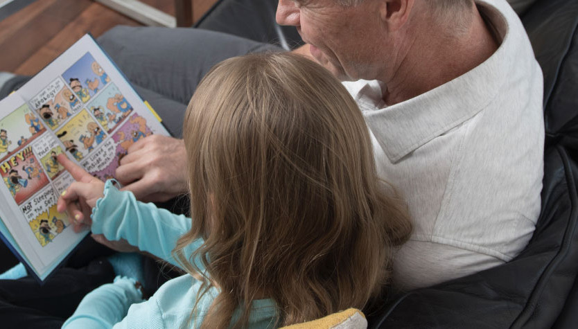 A man and a girl read a book together while sitting on a couch.
