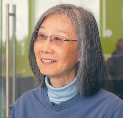 Rowena Liu-Poon sits outside a library meeting room with a glass door.