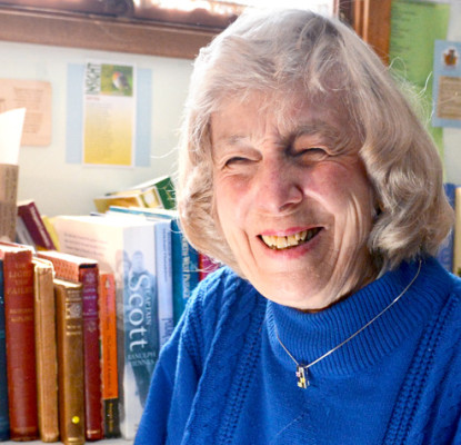 Norma High in the Calgary Public Library in front of books on shelves.
