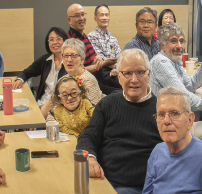 Photograph of a group of people all sitting at tables smiling at the camera. 