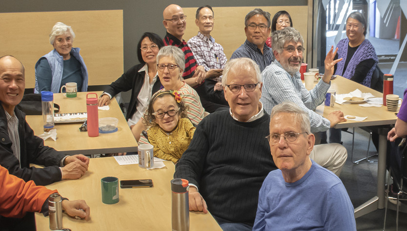 Photograph of a group of people all sitting at tables smiling at the camera. 
