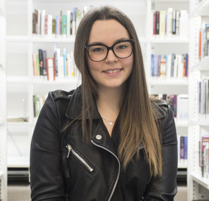 Steph Mok sitting in front of library shelves with books.