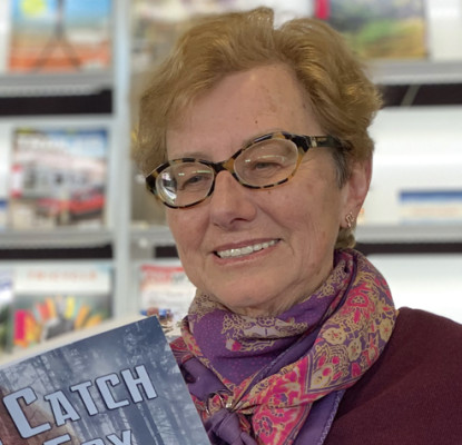 Susan Calder holding a book standing in front of a bookshelf.