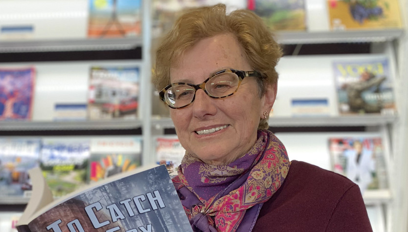 Susan Calder holding a book standing in front of a bookshelf.