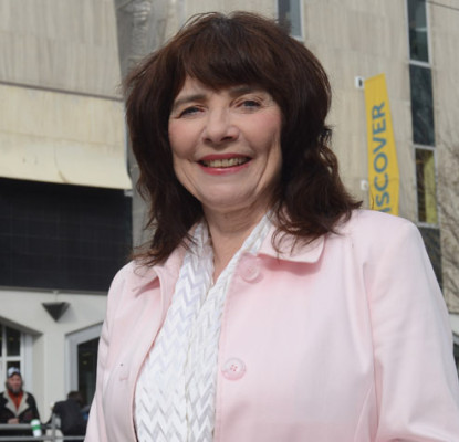Photograph of Marian Erb standing in front of a building with a large grey sign that reads "Calgary Public Library."