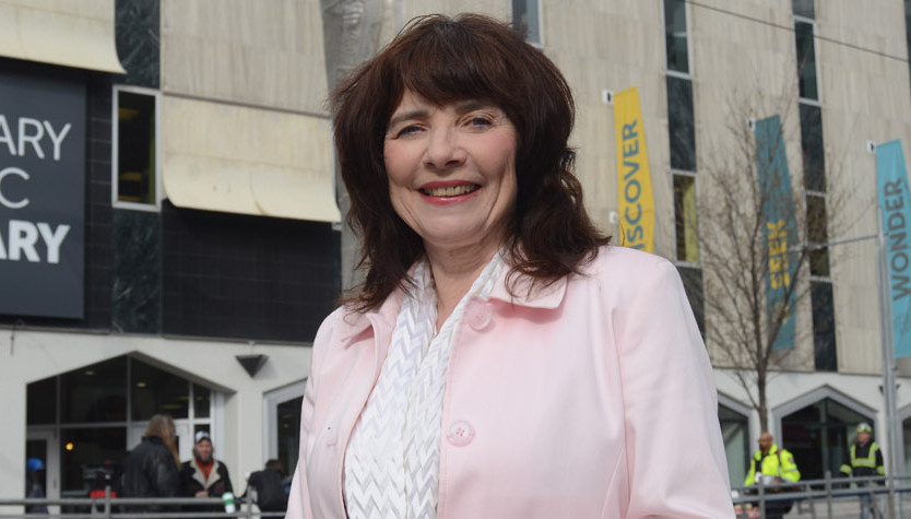 Photograph of Marian Erb standing in front of a building with a large grey sign that reads "Calgary Public Library."
