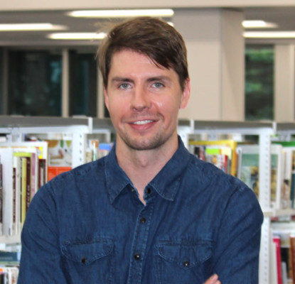 Photograph of Jesse Campbell standing in front of bookshelves. 