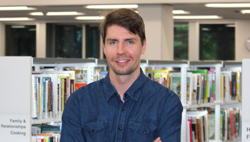 Photograph of Jesse Campbell standing in front of bookshelves. 