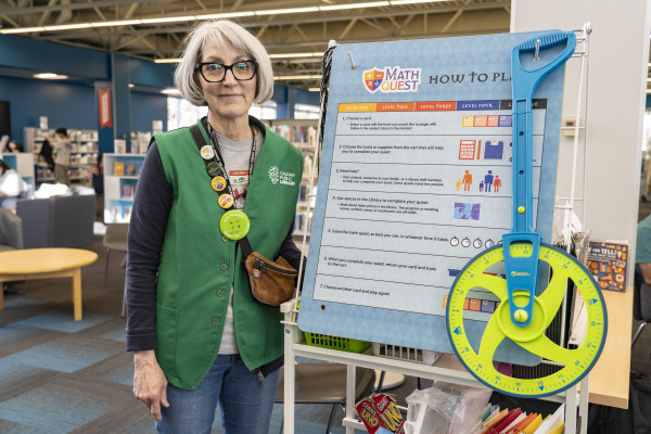 A Calgary Public Library volunteer standing beside an activity on a stand.