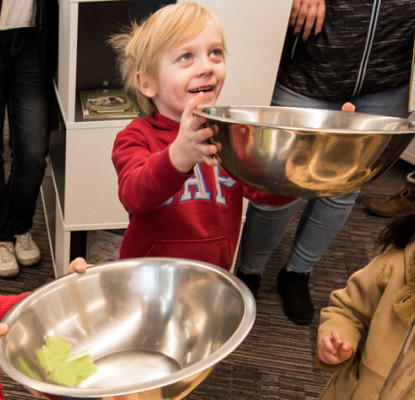 Photograph of three children. Two of the children pictured are holding large stainless steel bowls. 
