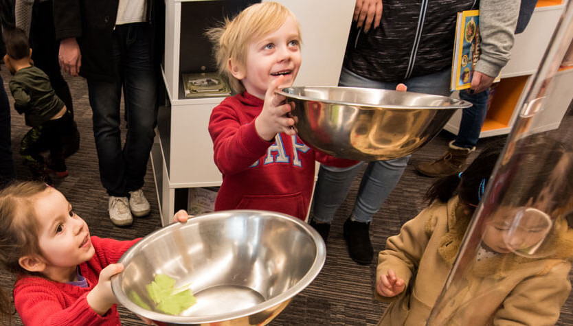 Photograph of three children. Two of the children pictured are holding large stainless steel bowls. 