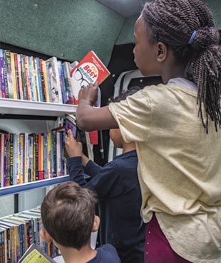 Children selecting books inside a book truck.