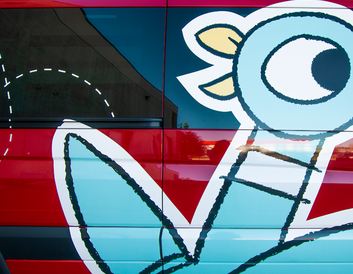 background image: A bright red vehicle with a large blue cartoon pigeon on the side.
