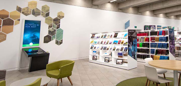 A photography of Calgary's Story. On the left hand side there is a display that says "Glimpses of Our Past" with different images in a hexagon format above it. On the right side is a row of bookshelves with Calgary's  Story written on the side of them.