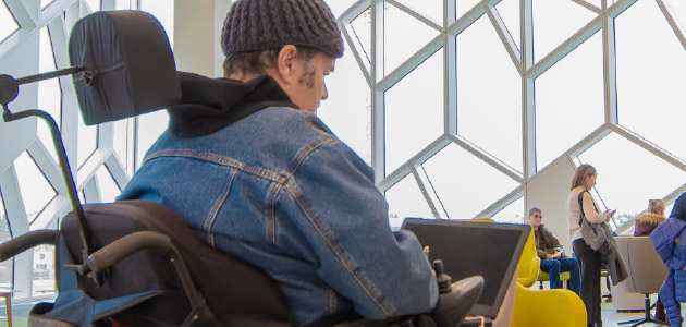 A person in a wheelchair using a laptop in a busy library.