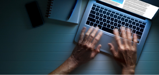 A pair of hands that are blurred are using a laptop.