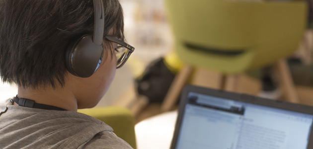 A photography of a kid wearing headphones and working on a computer.