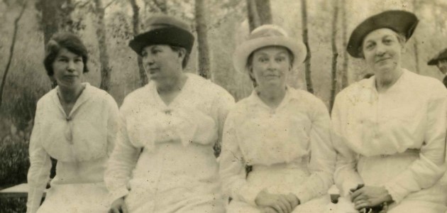 An old photograph of four ladies sitting. They are staring at the camera with slight smiles on their faces.