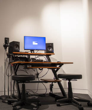 In the photograph, there is a computer set-up with audio equipment such as speakers and a microphone.