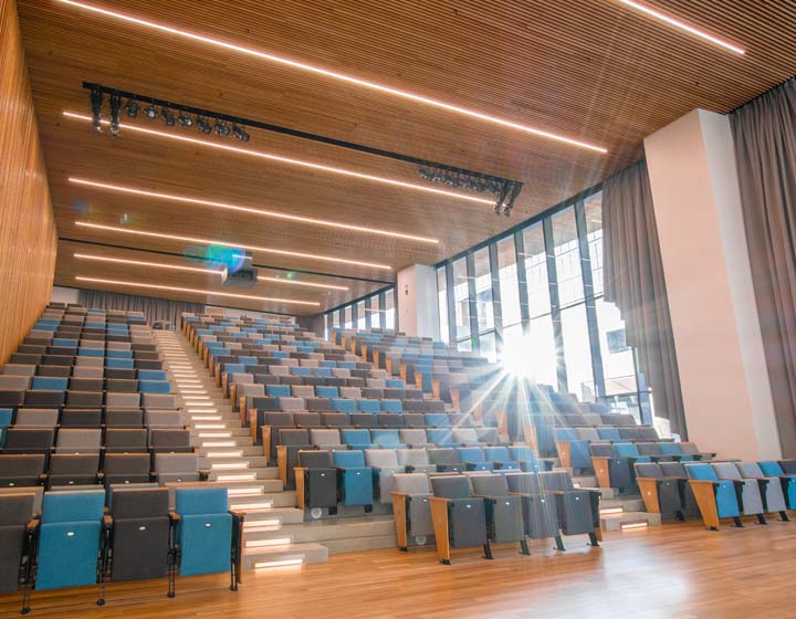 background image: A photograph of the Patricia A. Whelan Performance Hall. In the photo, the chairs are set up in an auditorium-style format.