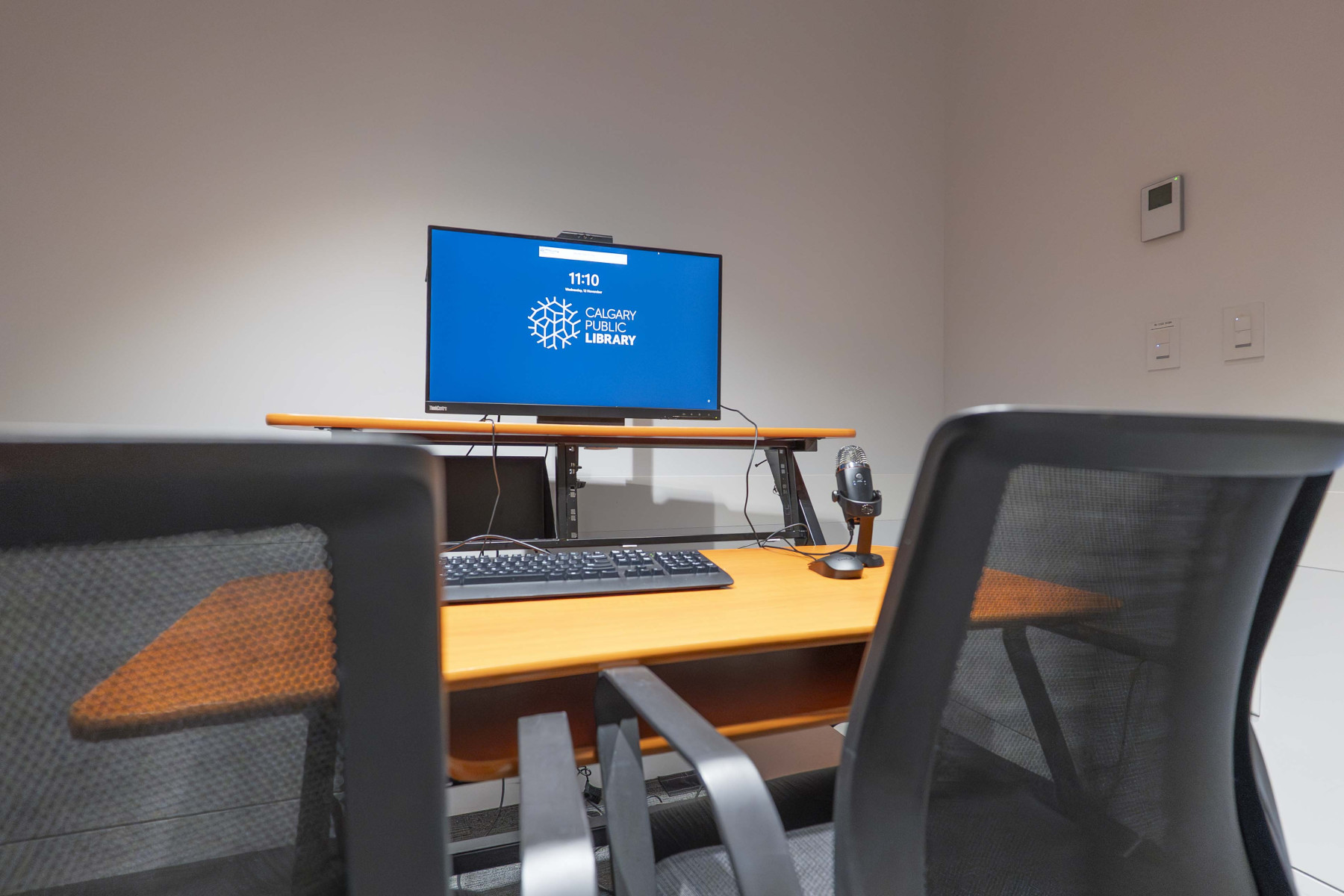 background image: A desk in a small room with a monitor, a computer, and two chairs