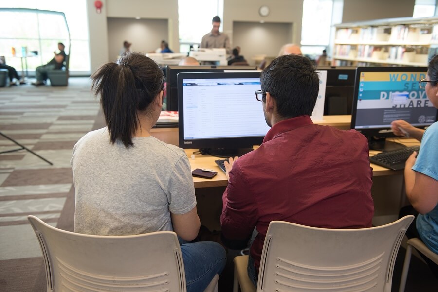 background image: Photo of two people working at a desk top computer. 