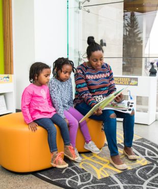 A woman and two children read a storybook together.