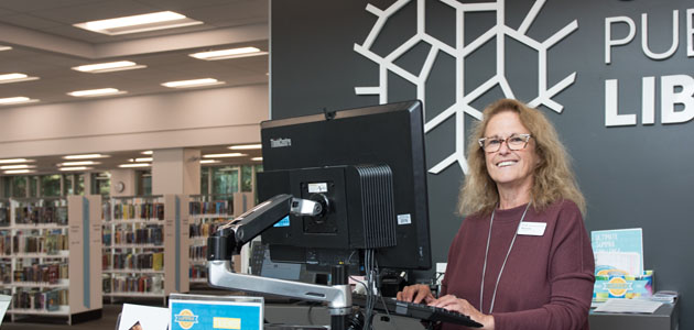 A smiling staff member stands at a Calgary Public Library service desk