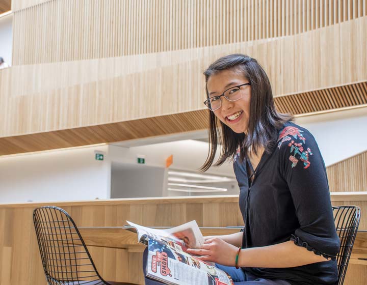 background image: A young woman sits at a table with a book in a library.